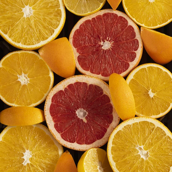 citrus fruits cut into slices laid out in the form of a heart on a black background, top view, copy space, square frame for Instagram