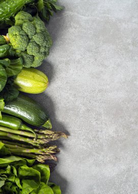 Yemek konsepti. Sadece gri taşlı arka planda yeşil sebzeler var. Dikey çerçeve, üst görünüm, sağdaki boşluğu kopyala.