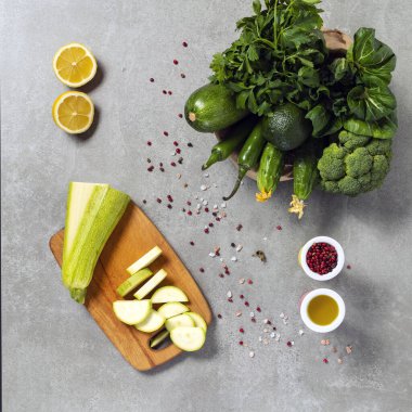 Yemek konsepti. Gri taştan bir arka planda yeşil sebzeler, limonlar, biberler, zeytinyağı. Instagram iletisi, kare çerçeve, üst görünüm