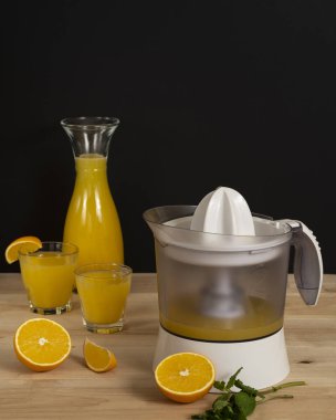 Cam kavanozdaki portakal suyu ve ahşap masadaki taze portakal dilimi.