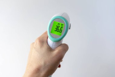 Bir kadın eli skor tabelasında bir termometre tutar. 36.6 santigrat derece görünür, sarı arka planda, yakın planda.