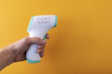 Bir kadın eli skor tabelasında bir termometre tutar. 36.6 santigrat derece görünür, sarı arka planda, yakın planda.