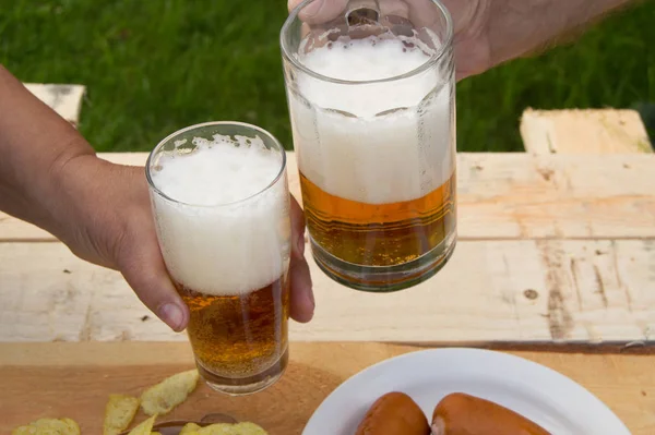 Manos Sosteniendo Vasos Con Cerveza Papas Fritas Salchichas Tumbadas Una — Foto de Stock