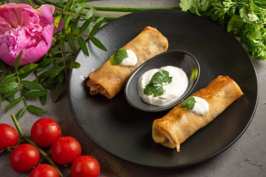 Kremalı ve ekşi kremalı pankekler yeşil ve domateslerle süslenmiş siyah tabakta.