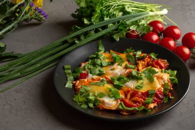 Domatesli sahanda yumurta ve siyah tabakta otlar.