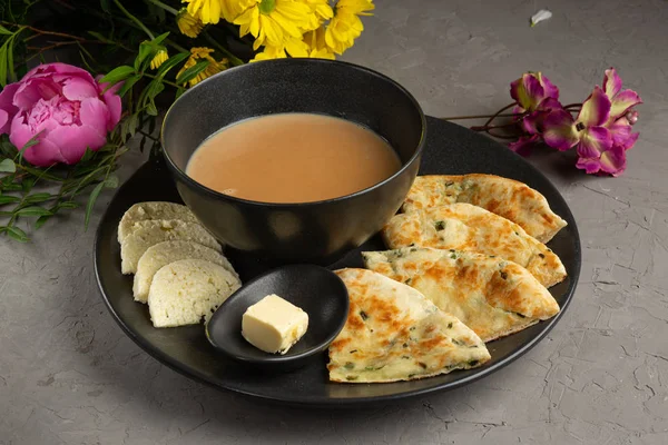 Kalmyk te i en kopp, fetaost, en paj med örter och en skiva smör i en svart tallrik Stockfoto
