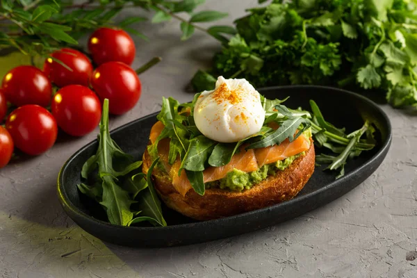 Bruschetta lax med avokado - saltad lax med guacamole, ruccola och pocherat ägg på en varm stekt bulle Royaltyfria Stockfoton