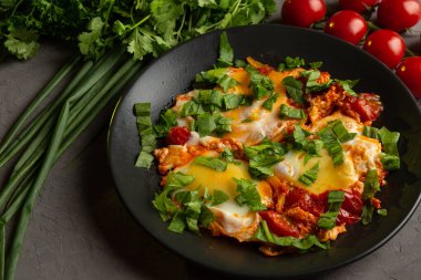 Domatesli sahanda yumurta ve siyah tabakta otlar.