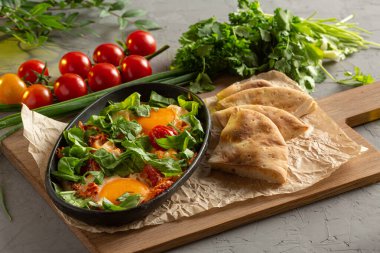 Oval siyah bir tabakta domatesli sahanda yumurta ve bitki.