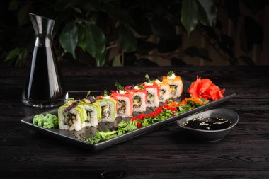 Yuvarlak bir tabakta suşi rulosu ve koyu ahşap arka planda soya sosu.