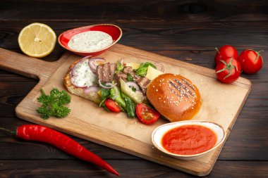 Kızarmış biftek, taze sebzeler, yeşillikler ve tahta bir tahta üzerinde ekmek.
