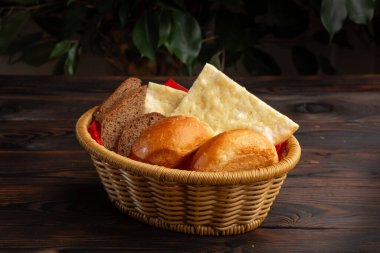 Koyu ahşap bir arka planda sepetteki çeşitli ekmekler.