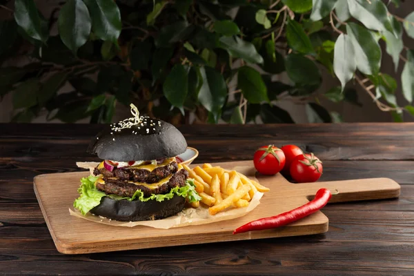 blackburger black mamba with marbled beef with french fries, chili pepper and tomatoes on a wooden board on a wooden table