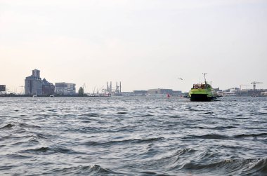 Tek bir gemiyle sakin su manzarası ve ufukta sanayi bölgesi, Amsterdam 