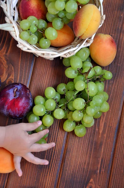 Olgun yeşil üzümler, kayısılar ve tahtadan arka planda çocuk eli olan erik, seçici bir odak noktası. 