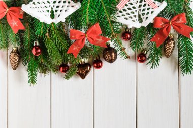 Üst manzara, ladin dalları, yeni yıl oyuncakları ve beyaz ahşap arka planda fiyonklar.