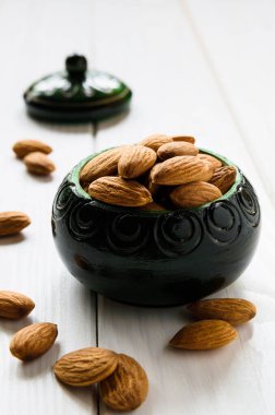 Yakın plan, bademler yeşil ahşap bir kasede beyaz bir masa üzerinde.