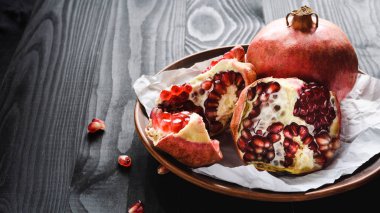 Yakın plan, olgun narlar kahverengi bir kâse üzerinde siyah bir ahşap masada.