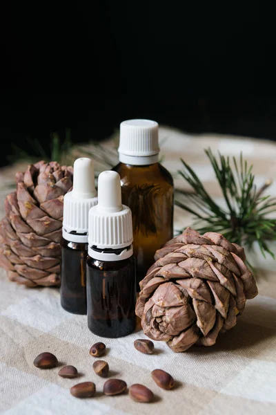 Producto natural, botellas de vidrio con aceite, conos de pino con nueces en un mantel sobre un fondo negro, primer plano — Foto de Stock