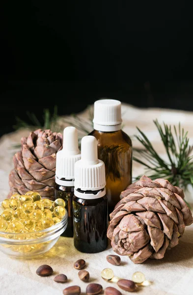 Producto natural, botellas de vidrio con aceite, conos de pino con nueces en un mantel sobre un fondo negro, primer plano — Foto de Stock