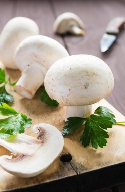 Durgun bir hayat, ahşap bir masanın üzerindeki kesme tahtasındaki otlu şampiyon mantarlar.