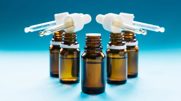Cosmetología, botellas de vidrio con pipetas y cosméticos sobre fondo azul —  Fotos de Stock