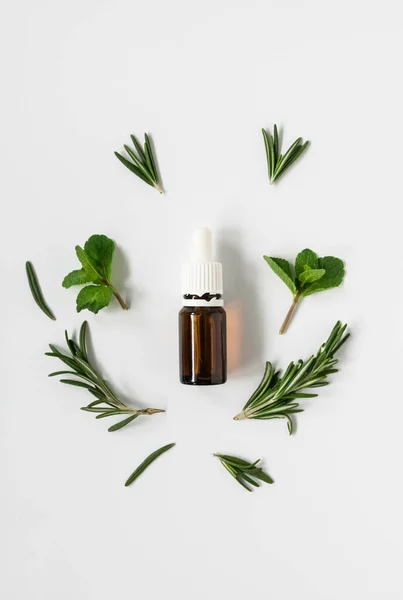 Frascos de vidrio con aceites esenciales y hojas de romero y menta sobre un fondo blanco, espacio libre para texto — Foto de Stock