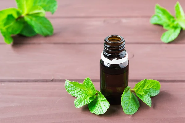 Bottle with essential oil and mint leaves on a brown wooden table — Stock Photo, Image