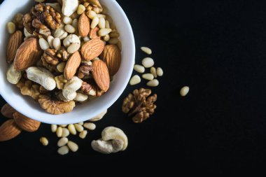 Süper yiyecek kavramı, badem, sedir, ceviz, fındık, siyah arka planda bir tabakta.