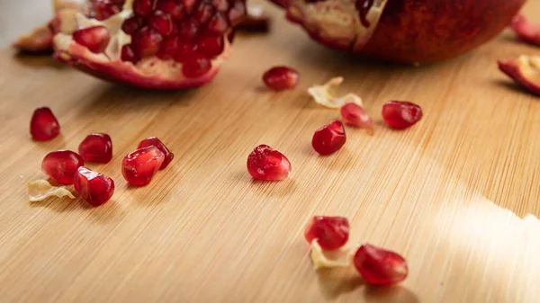 Grains of red ripe pomegranate on a wooden board on a table — Stock Photo, Image