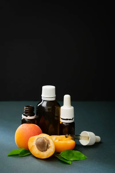 Konsep kosmetik alami, aprikot dengan botol kaca dengan minyak di latar belakang gelap — Stok Foto