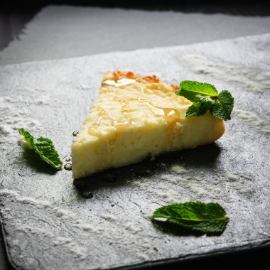 Peynirli kek üzerine şeker serpilmiş ve üzerine nane yaprakları serpiştirilmiş.