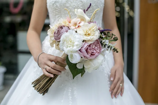 De bruid in de witte jurk en een bos bloemen in haar hand — Stockfoto
