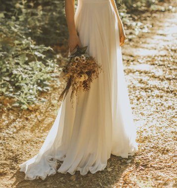 Beyaz elbiseli gelin ve elinde bir demet çiçek.