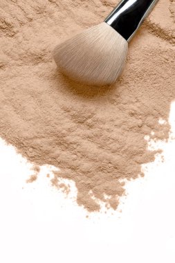 Kozmetik ve güzellik kavramında yumuşak kıllı makyaj fırçasıyla beyaz bir zemine dağılmış gevşek kozmetik tozu.