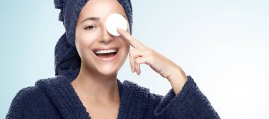 Güzellik ve cilt bakımı. Temiz bir ciltle gülümseyen sağlıklı genç bir kadın makyaj temizliği ve günlük güzellik yüz temizliği kavramında makyaj malzemesi için göz göze pamuk tutuyordu. Mavi arkaplan