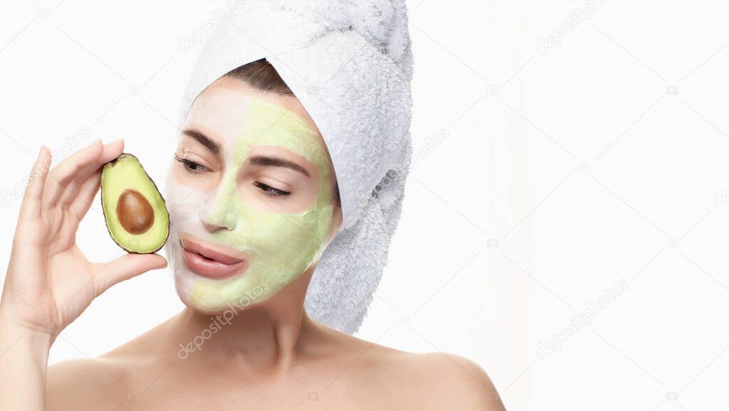 Spa woman with facial beauty mask and half fresh avocado in hand. Beautiful brunette with a towel on head using a facial mask treatment. isolated on white with copy space. Beauty & Skin care concept
