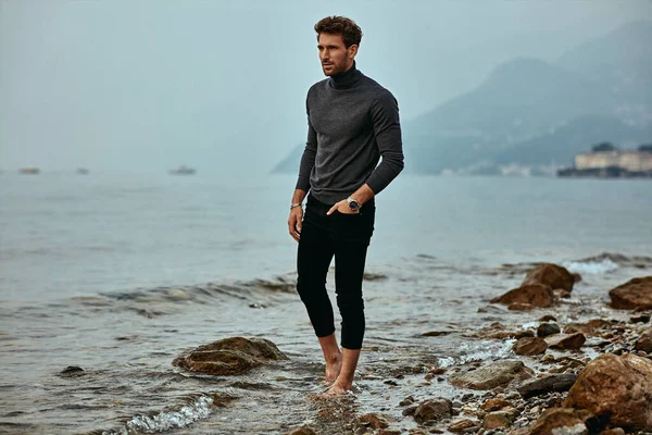 Schöner Mann trägt modische Kleidung, geht am Strand spazieren und — Stockfoto
