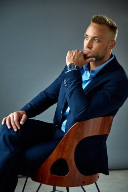 Young elegant man in blue suit touching chin and thinking 