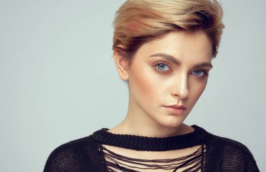 Mavi gözlü ve gri arka planda izole edilmiş kısa sarı saçlı genç kadın modelin yüzünü kapatın.