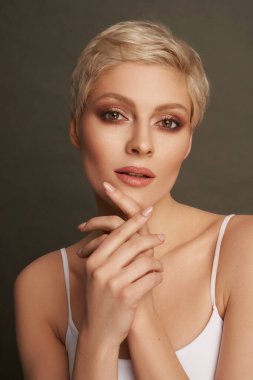Portrait of sexy blonde in short hair applying cream on hads isolated on gray background clipart