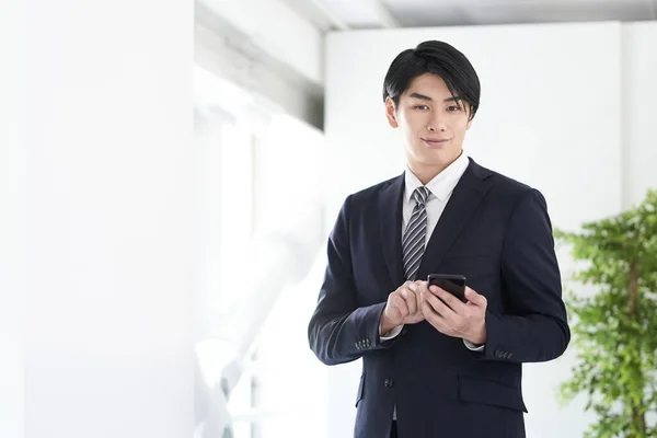 A Japanese male businessman uses his smartphone with a smile on his face