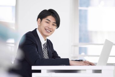Japon bir erkek işadamı dizüstü bilgisayarında çalışırken gülümsüyor..