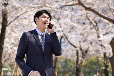 Japon bir işadamı arka planda kiraz çiçekleriyle telefon görüşmesi yapıyor..