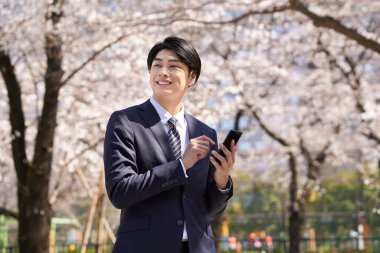 Japon bir işadamı arka planda kiraz çiçekleriyle telefon görüşmesi yapıyor..