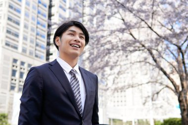 Gülümseyen bir Japon işadamı, bir ofis bölgesinde kiraz çiçeklerinin önünde duruyor..
