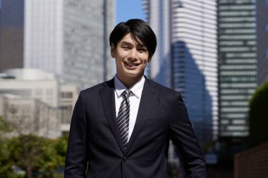 Bir ofis bölgesinde gülümseyen bir Japon erkek işadamı duruyor..