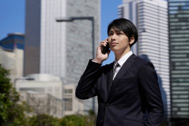 Japon bir erkek işadamı bir ofis bölgesinde telefon görüşmesi yapıyor.