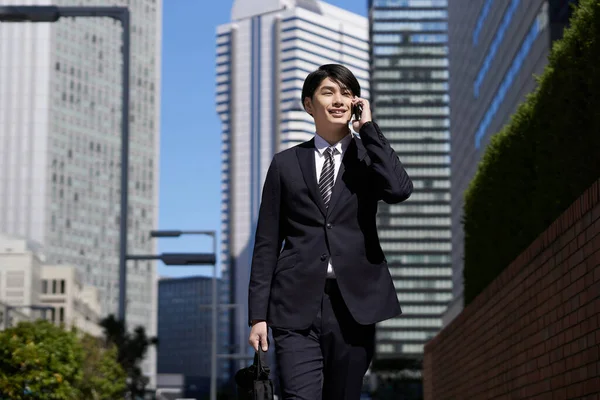 A Japanese male businessman making a phone call in an office district