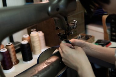 Bir kadının eli dikiş makinesiyle deri dikiyor.